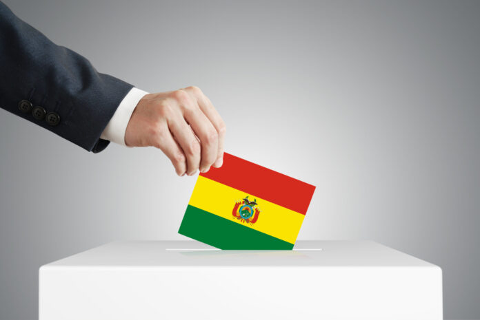 Man putting a voting ballot into a box with Bolivian flag.